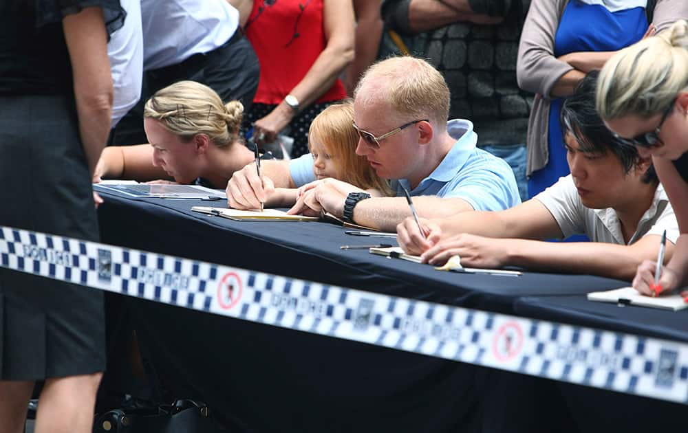 People sign tributes at a makeshift memorial after shootings during a siege at the Lindt Chocolat Cafe at Martin Place.
