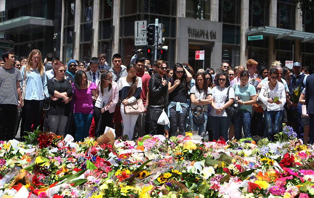 Staff members from the Lindt Chocolat Cafe with their arms linked pay tribute to their colleague who lost his live during a siege at the popular coffee shop at Martin Place.