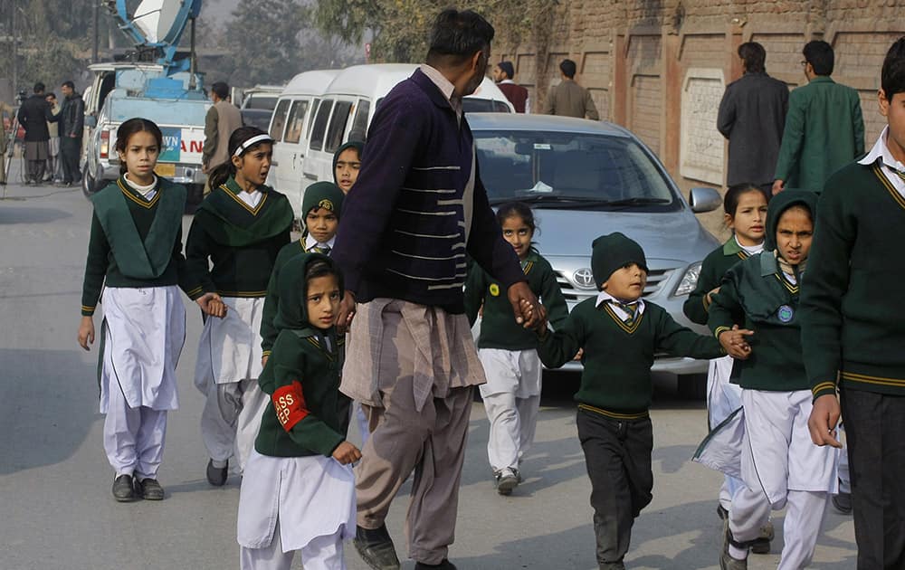 A plainclothes security officer escorts students rescued from nearby school during a Taliban attack in Peshawar, Pakistan.