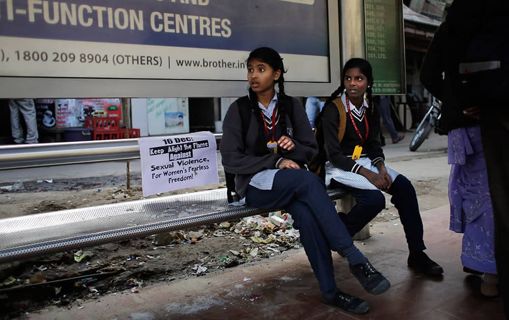 Indian schoolgirls sit next to a placard at a bus stop where the victim of a deadly gang rape in a moving bus had boarded the bus two years back, in New Delhi, India, Tuesday.