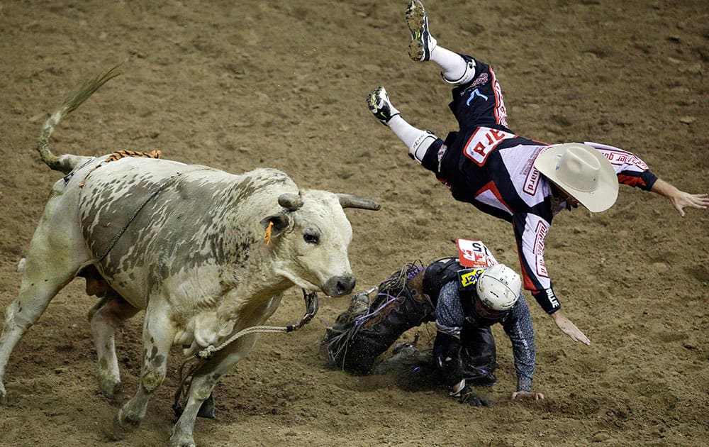 Bullfighter Chuck Swisher, top, gets tossed into the air by bull Cajun Smurf while Swisher was protecting Bull rider Trey Benton III during the seventh go-round of the National Finals Rodeo, in Las Vegas.