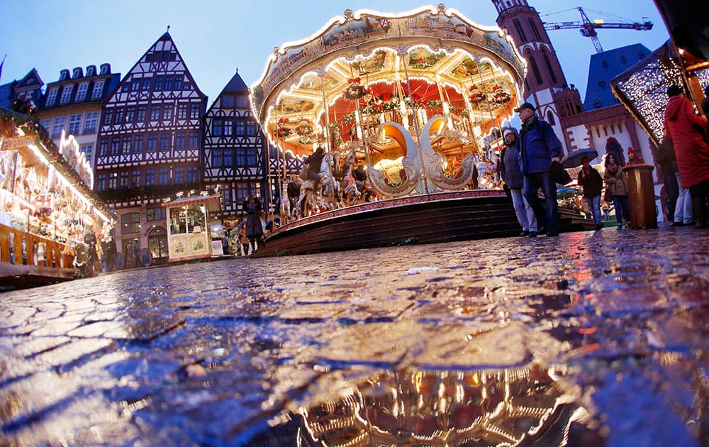 The merry-go-round of a Christmas market is reflected in a puddle on a rainy afternoon in Frankfurt, Germany.