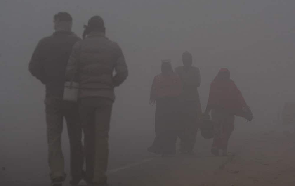 Indians, wrapped in warm clothes, walk through a fog covered road in Jammu, India. As winter sets in, thick fog engulfs most of north India disrupting normal life. 