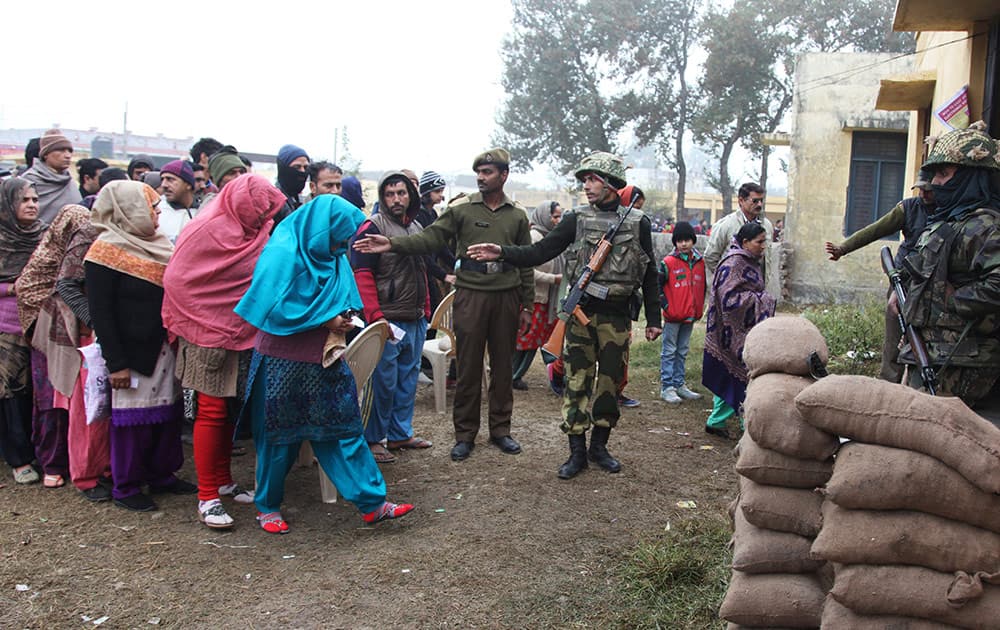 Paramilitary soldiers stand guard, as people stand in queues to cast their votes outside a polling station during the fifth phase of voting, at Satrayan village, Jammu.