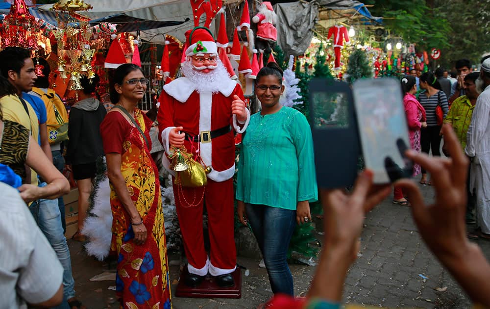 People stand to take a photograph beside a decorative Santa Claus for sale at a market in Mumbai.