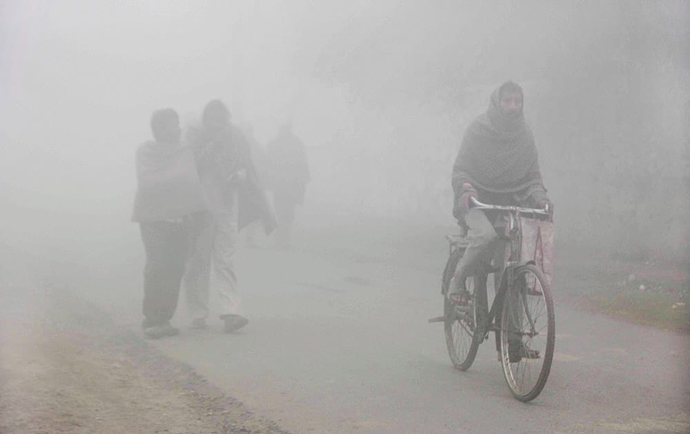 People wearing warm clothes move on the road on a chilly foggy morning as the temperature fell down in Allahabad.