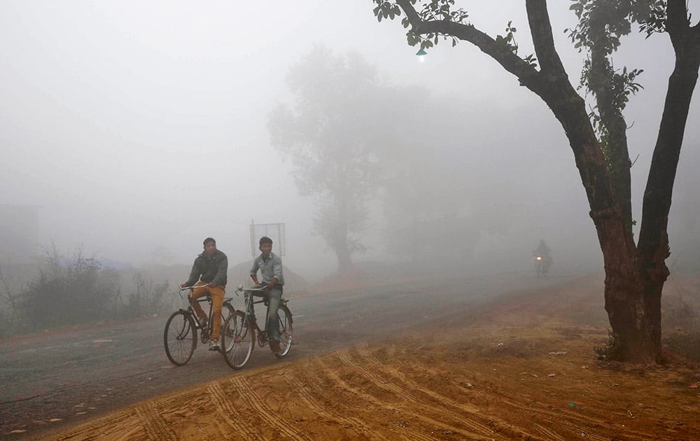 Indian villagers cycle amidst fog early morning in Allahabad.