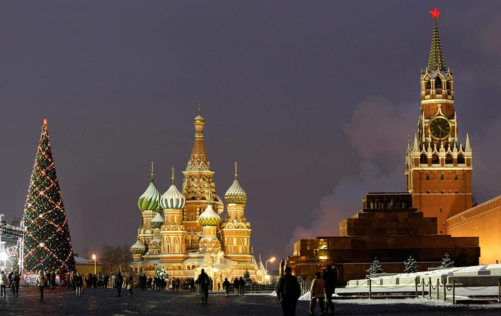 In this photo people walk past a huge Christmas tree installed in Red Square, with St. Basil Cathedral, center, the Kremlin's Spassky Tower, right back, and Lenin Mausoleum, right, in Moscow, Russia.