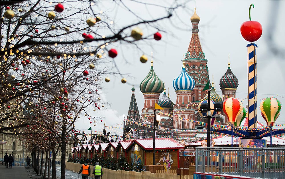 Municipal workers walk along a fence surrounding a Christmas market at Red Square with St. Basil's Cathedral in the background in Moscow, Russia.