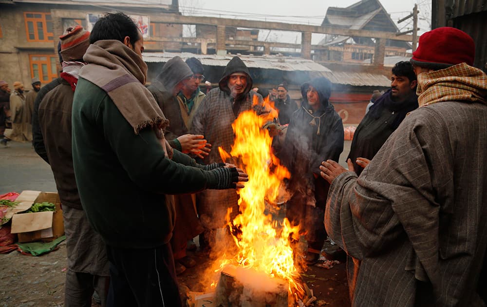 Kashmiri men warm their hands standing near a bonfire on a cold and foggy morning in Srinagar.