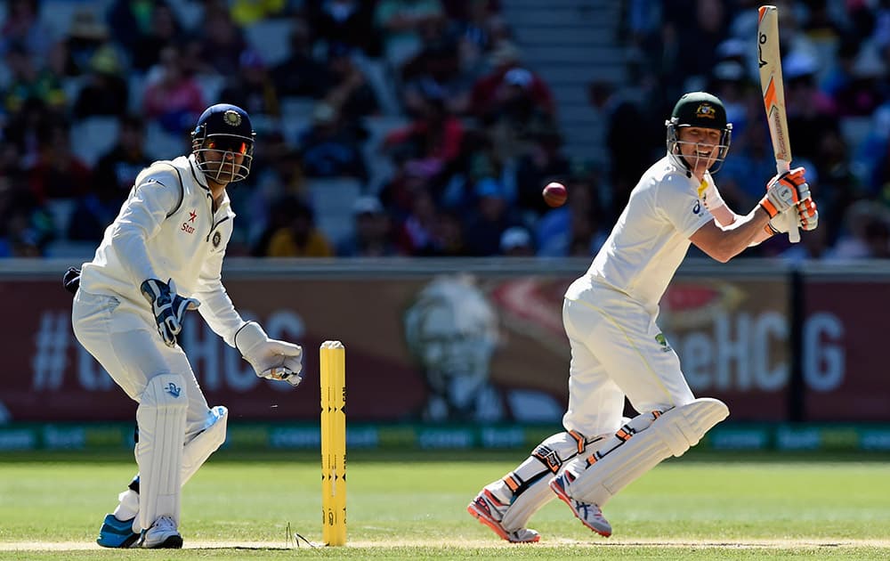 Australia's Brad Haddin, hits a cut shot as India's MS Dhoni, watches on during their play on day one of the third cricket test in Melbourne, Australia.