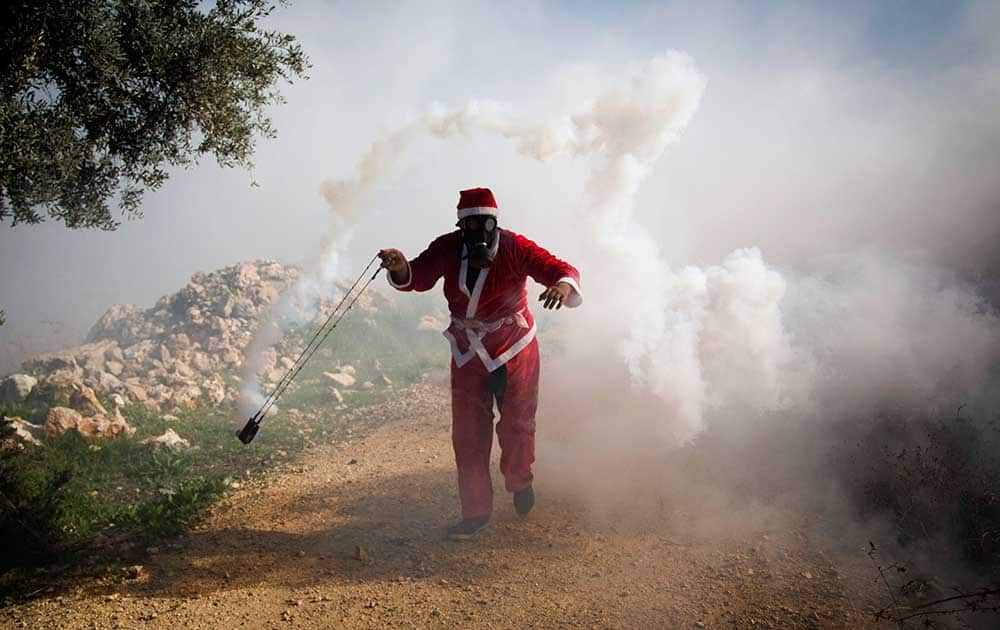 A Palestinian protester wearing a Santa Claus costume uses a sling to throw back a tear gas canister fired by Israeli soldiers during a protest against Israel's separation barrier outside the West Bank village of Bilin, near Ramallah.