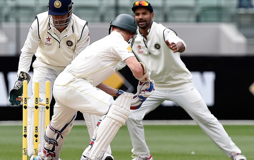 Australia's Chris Rogers, plays on to his stumps and is out for 69 runs as India's MS Dhoni, and Shikhar Dhawan look on during the fourth day of their cricket test match in Melbourne, Australia.