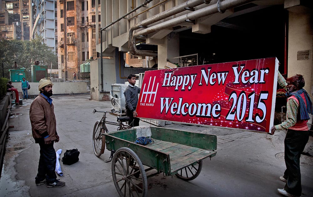 Laborers hold a billboard as they prepare to put it on display on a hotel building ahead of New Year 2015, in New Delhi.