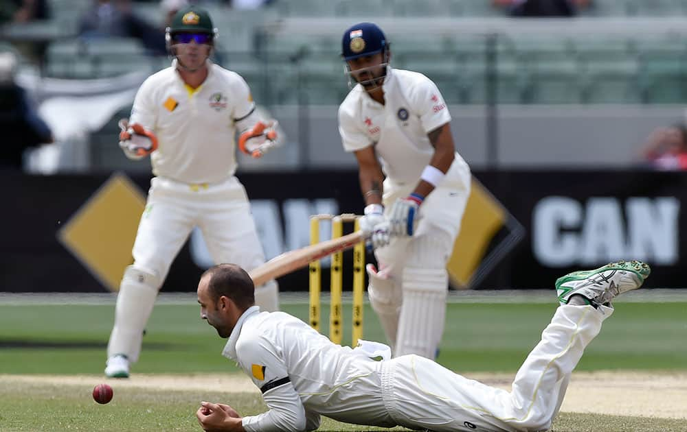 Australia's Nathan Lyon fields off his own bowling to India's Virat Kohli, right, on the final day of their cricket test match in Melbourne, Australia.