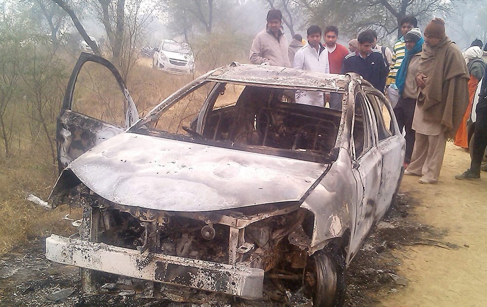 People look on damaged car in which four Delhi youth found charred inside the car at a village in Jhajjar district of Haryana.