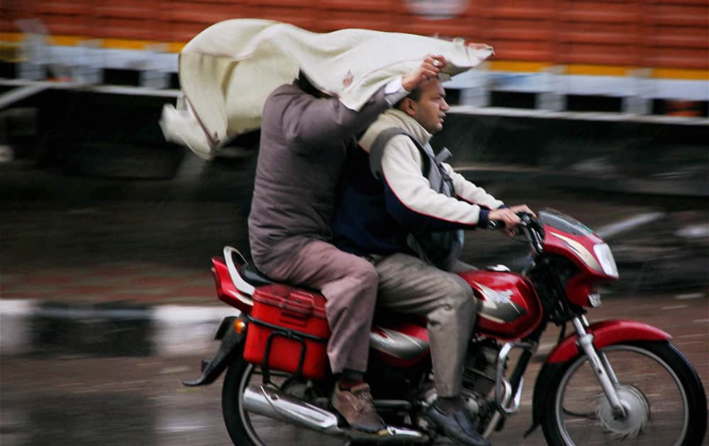 A person riding pillion on a bike attempts to shield the rider and himself from the early morning rain in New Delhi.