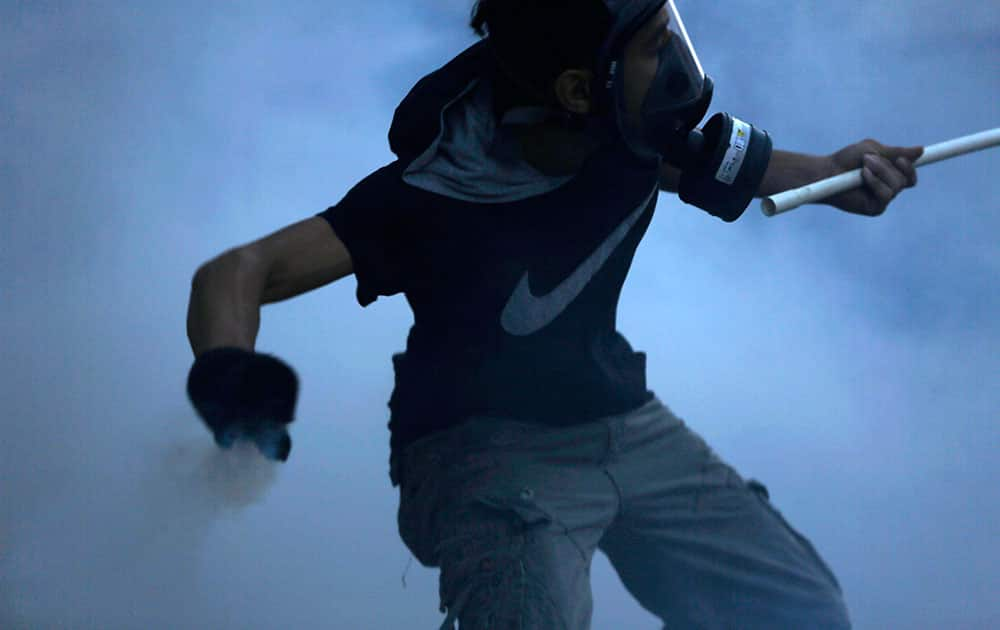 A masked Bahraini anti-government protester carrying a flag holds a tear gas canister he is preparing to throw back toward police who fired it during clashes in Bilad Al Qadeem, Bahrain, a suburb of Manama.