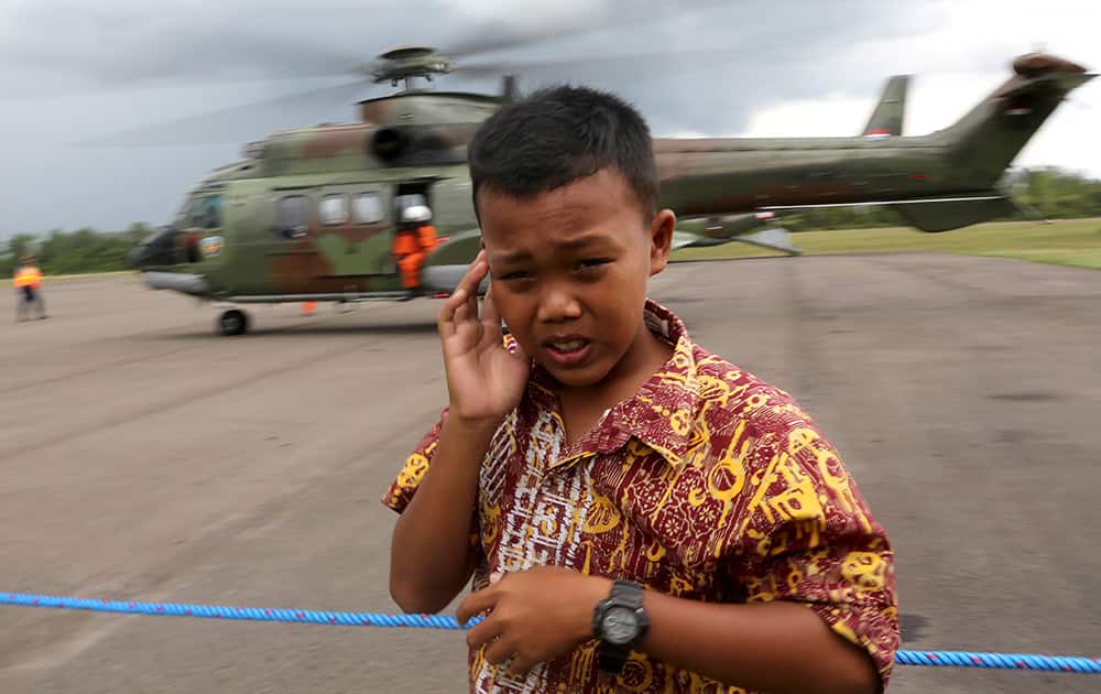 A child covers his ear as Indonesian Air Force's Super Puma helicopter lands after a search operation for the victims and the wreckage of AirAsia Flight 8501 at Pangkalan Bun Airport, Indonesia.