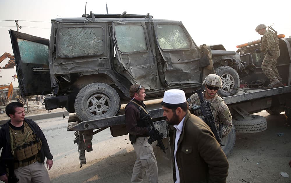 An Afghan man walks past foreign security forces searching a destroyed vehicle at the site of a suicide car bomb attack in Kabul, Afghanistan.