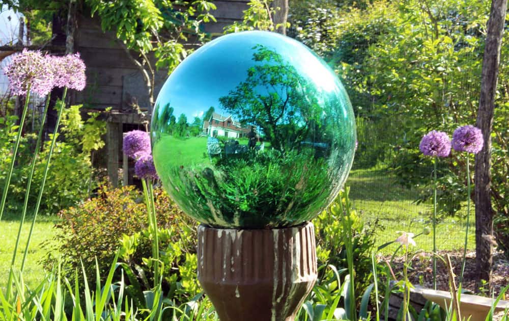 a green-tinted gazing globe visually takes in all of last summer’s garden in New Paltz, New York. These mirrored glass ornaments fell out of favor about 50 years ago, but are making a comeback, seen by some as attractive ornaments and by others as kitsch.