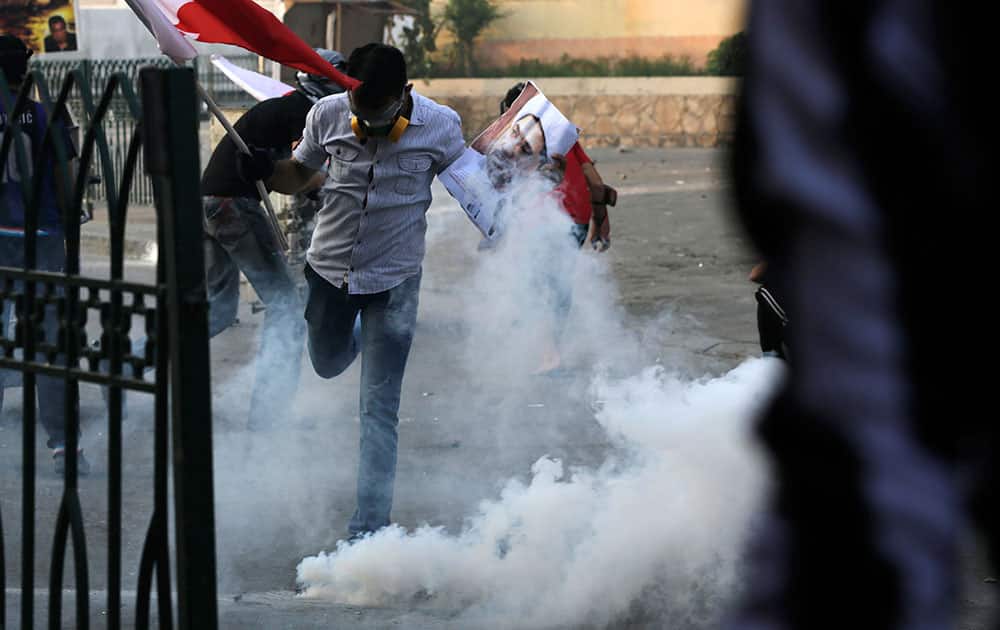A masked Bahraini anti-government protester, holding a national flag and a picture of Shiite opposition leader Sheik Ali Salman, kicks away a tear gas canister fired by police during clashes in Bilad Al Qadeem, Bahrain, a suburb of Manama.