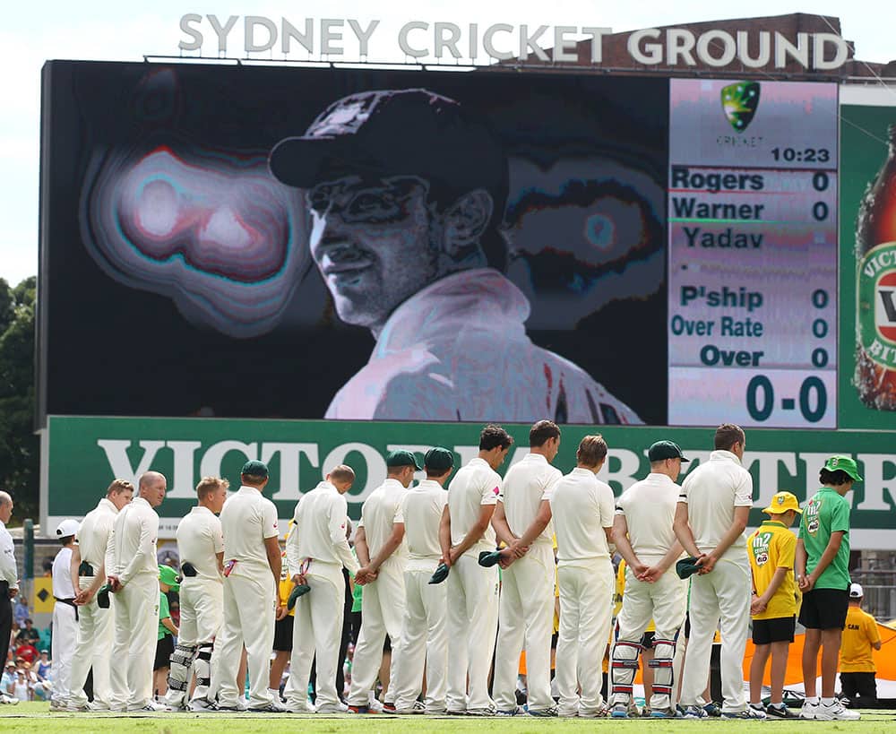 Australian teammates pause for a moment at the Sydney Cricket Ground as a photo of their teammate Phil Hughes appears on a screen during the opening ceremony for their cricket test match against India in Sydney.