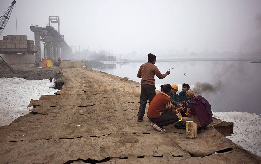 Construction workers sit by a fire to keep themselves warm on the banks of the Yamuna River on a foggy morning in New Delhi, India.