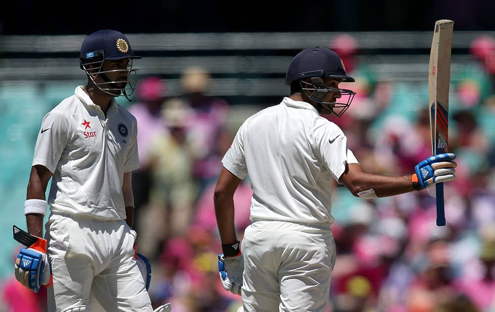 Rohit Sharma lifts his bat to celebrate making 50 runs against Australia as teammate Lokesh Rahul watches on the third day of their cricket test match in Sydney.