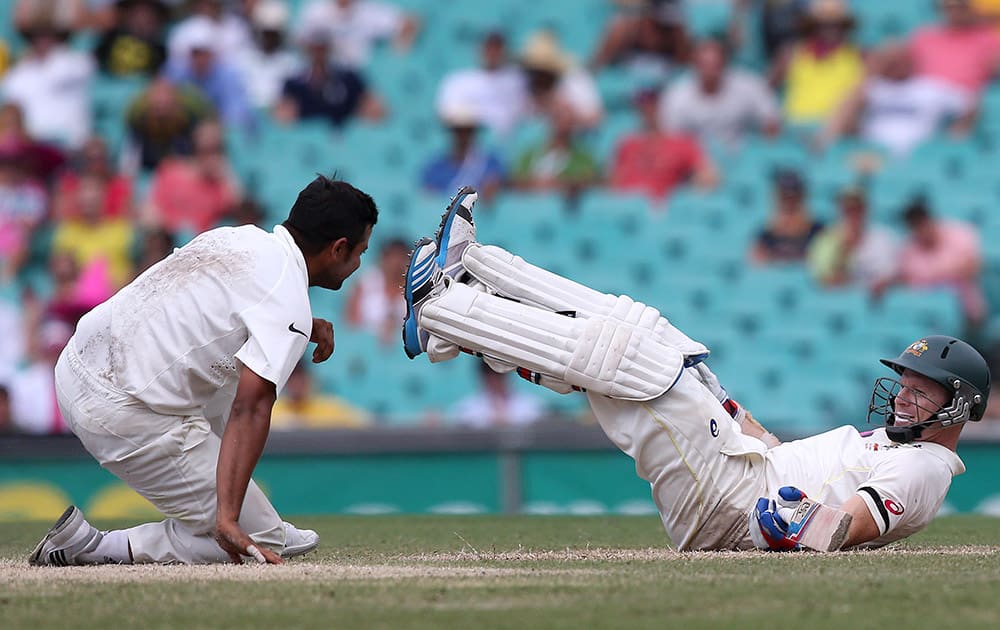 Australia's batsman Chris Rogers, and India's Suresh Raina fall to the ground after colliding on the pitch on the fourth day of their cricket test match in Sydney.