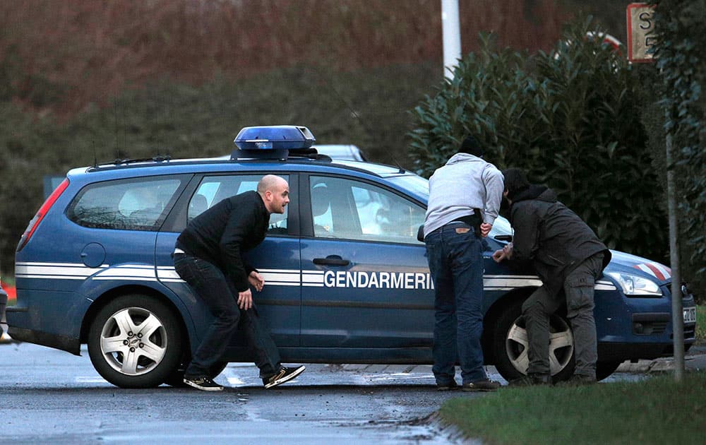 A police officer takes shelter behind a gendarme car in Dammartin-en-Goele, northeast of Paris, where the two brothers suspected in a deadly terror attack were cornered.