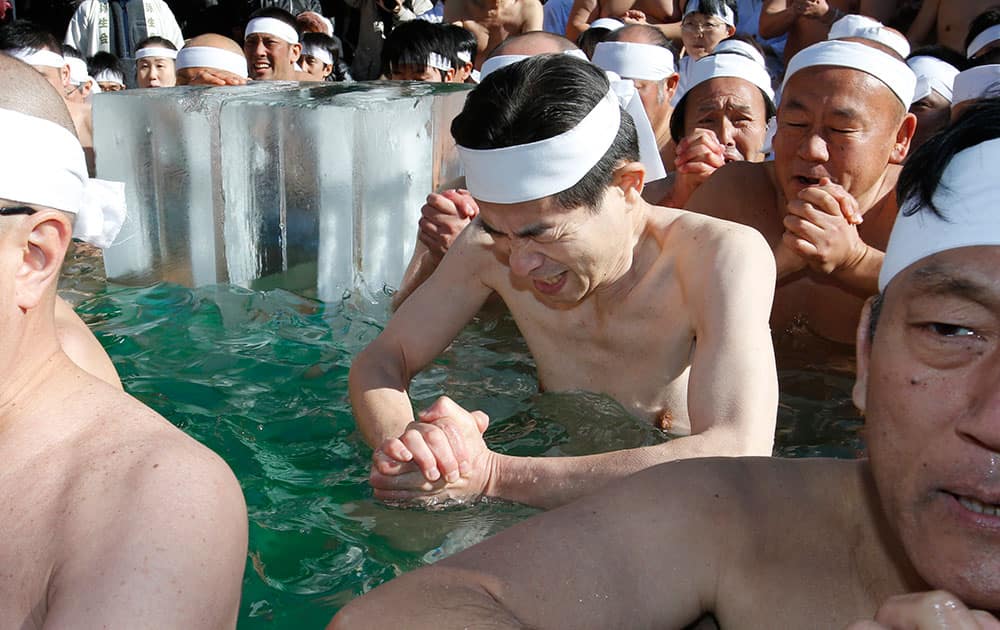 A Japanese bather grimaces as he prays with others for the healthy new year while dipping in a cold water tub with blocks of ice at Teppozu Inari Shinto Shrine during a winter ritual in Tokyo.