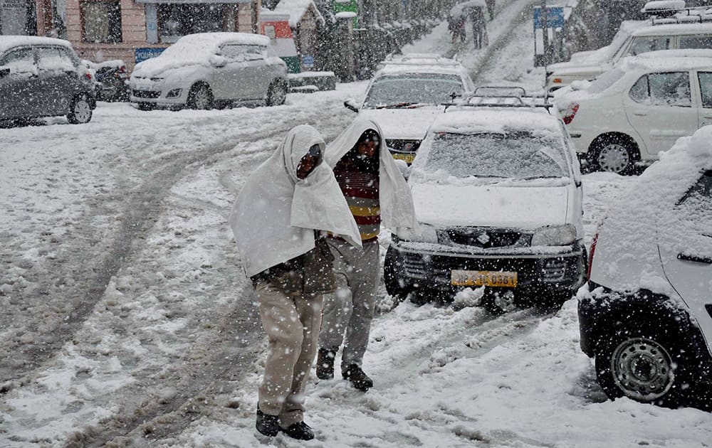 Blanket of snow forms over the roads and vehicles while people walk covered in warm clothes after snowfall in Dalhousie.