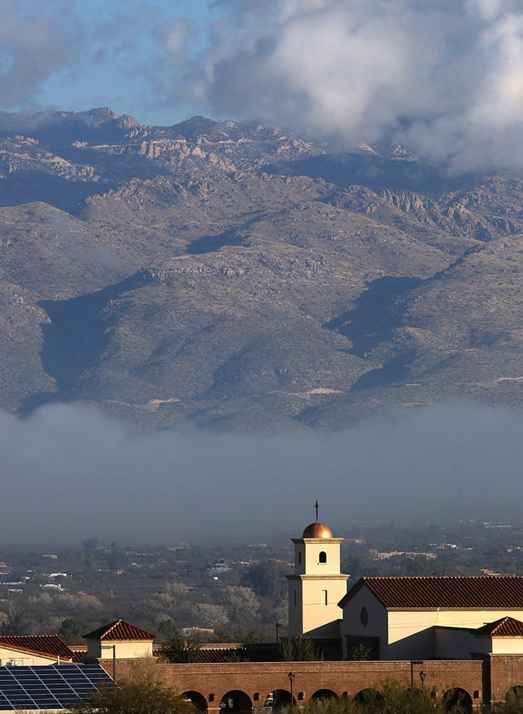 Heavy fog moves along the bottom of the Tucson valley as it partially lifts revealing parts of the Santa Catalina Mountains and the Corpus Christi Catholic Church in Tucson, Ariz.