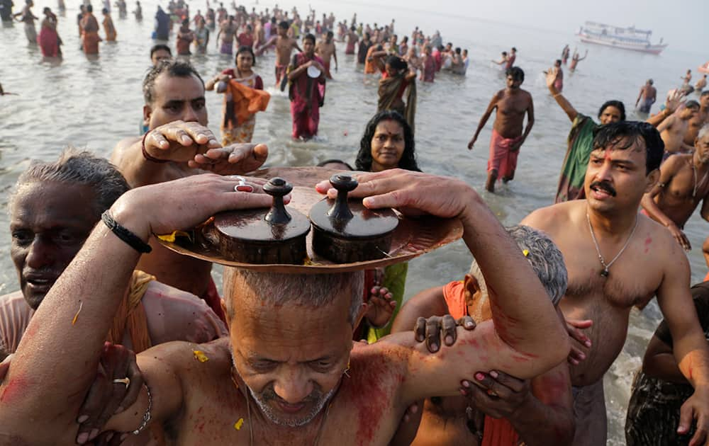 A Hindu devotee carries a pair of wooden slippers belonging to his late Guru, or spiritual teacher, on his head as a sign of respect after taking a holy dip to mark Makar Sankranti festival in Gangasagar.