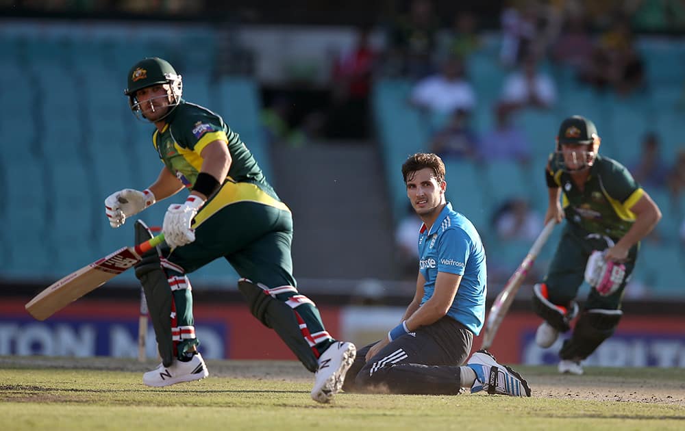 England's Steven Finn, watches from his knees as Australia's Aaron Finch and David Warner make runs during their One Day International cricket match in Sydney.