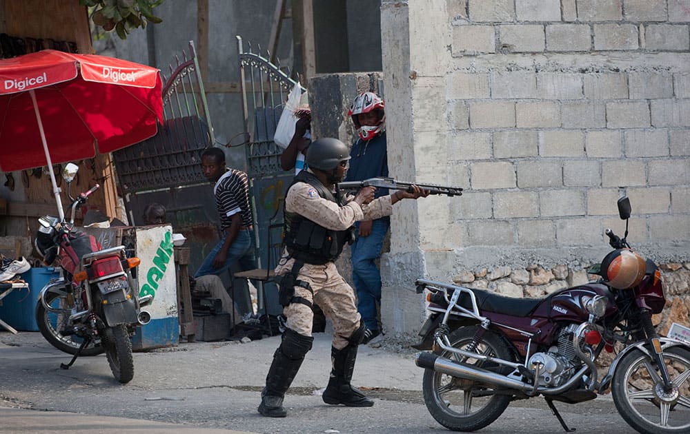 A National Police officer fires at protesters after clashes broke out with police during a demonstration to demand the resignation of President Michel Martelly, in Port-au-Prince, Haiti.