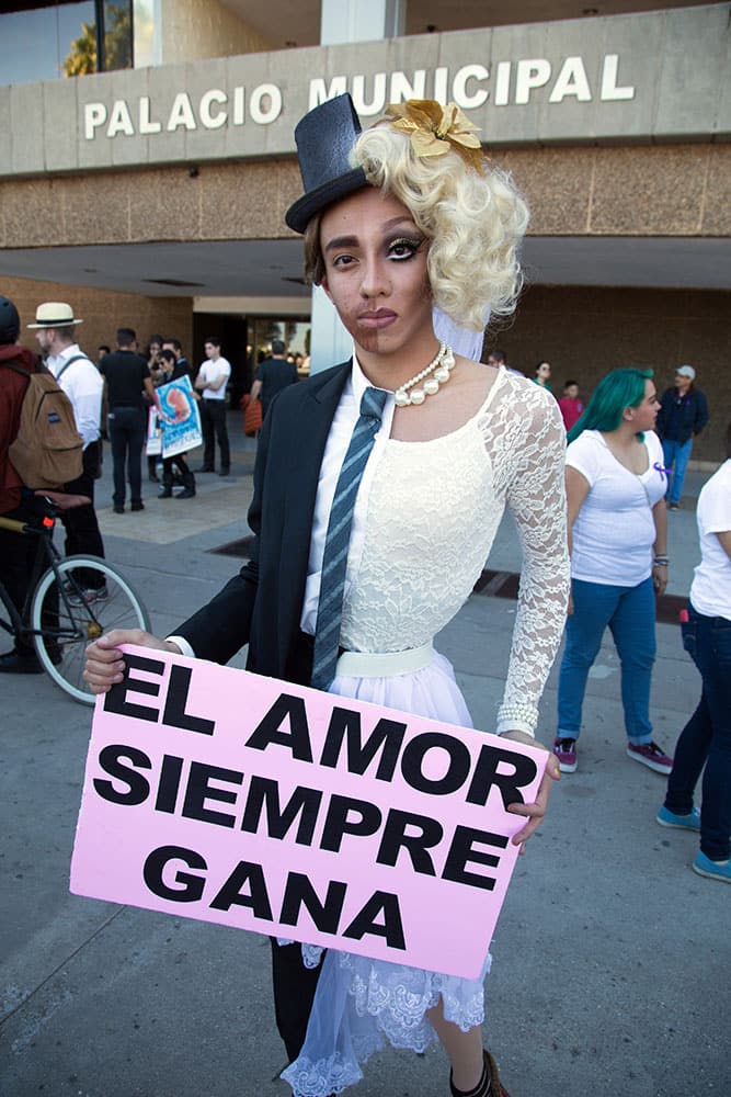 Antonio Yee of Los Angeles, California, 20, dressed as a half man, half woman, holds up sign with a message that reads in Spanish; 