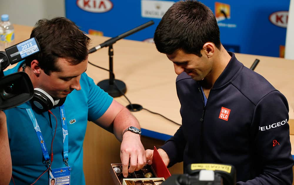 A reporter takes a chocolate from Novak Djokovic of Serbia, right, during a press conference at the Australian Open tennis championship in Melbourne, Australia, Sunday.