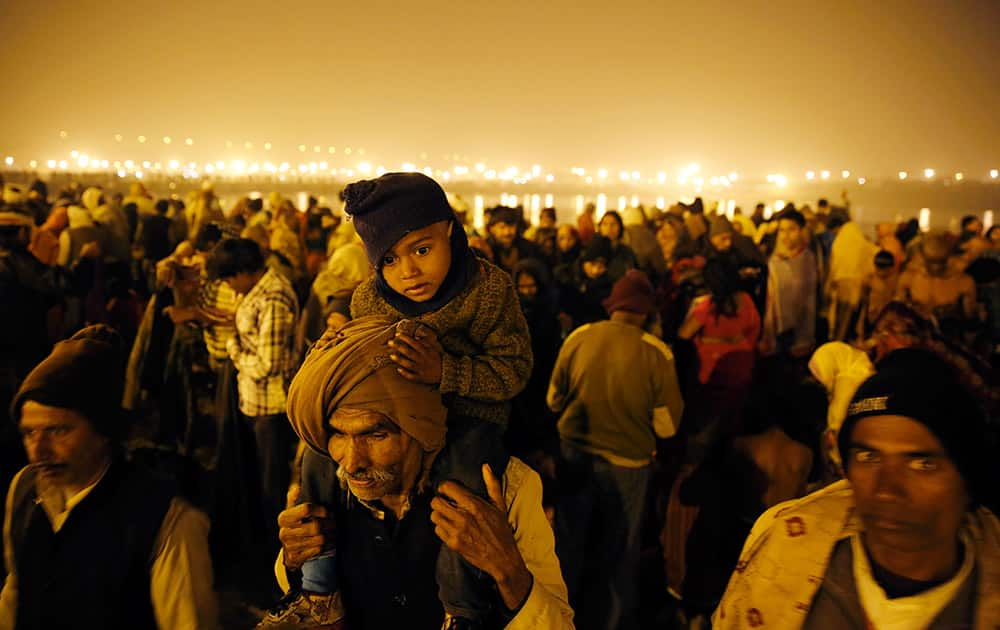 An elderly Indian Hindu devotee carries his grandson oh his shoulder as he and others arrive at the Sangam, the confluence of rivers Ganges and Yamuna, on 'Mauni Amavasya,' or new moon day, the third and the most auspicious date of bathing during the annual month long Hindu religious fair 'Magh Mela' in Allahabad.