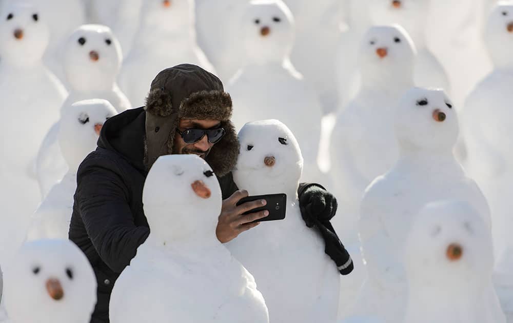 A man surrounded by snowmen takes a selfie with a cell phone during a protest against the Davos World Economic Forum, WEF, in Davos, Switzerland.