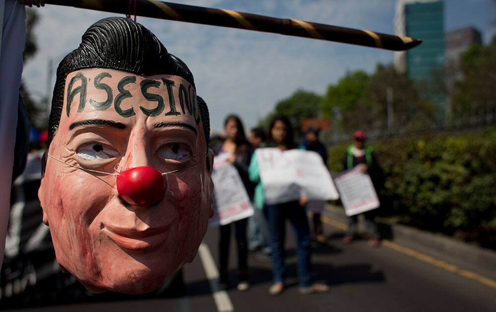 A protestor carries a hanging mask of Mexican President Enrique Pena Nieto marked with the word in Spanish 