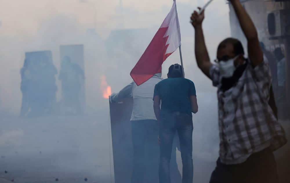 Bahraini anti-government protesters, some carrying national flags, stand behind makeshift shields facing riot police during clashes in a street full of tear gas in Bilad Al Qadeem, Bahrain.