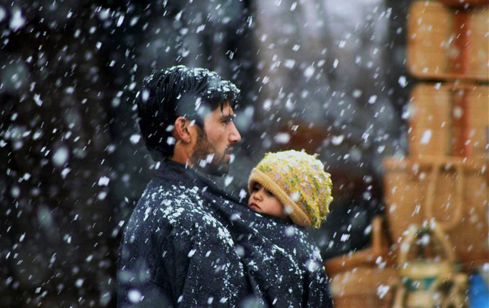 A Kashmiri man carries his daughter as he walks on a snow-covered road closed due to heavy snowfall at Qazigund in Anantnag district.