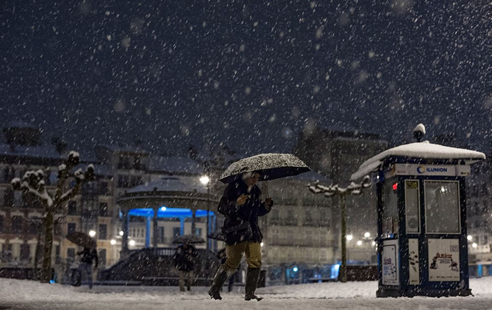 A woman crosses Plaza del Castillo square as the snow falls on a winter night, in Pamplona northern Spain. A cold spell has reached northern Spain with temperatures plummeting far below zero.