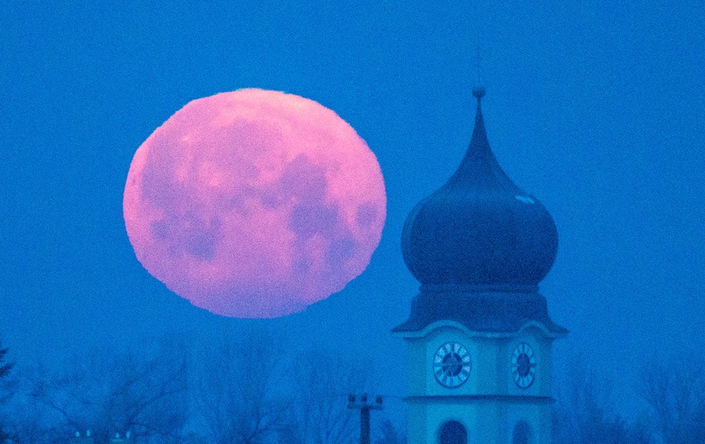 The moon sets behind the parish church of Schoenach near Regensburg, southern Germany.