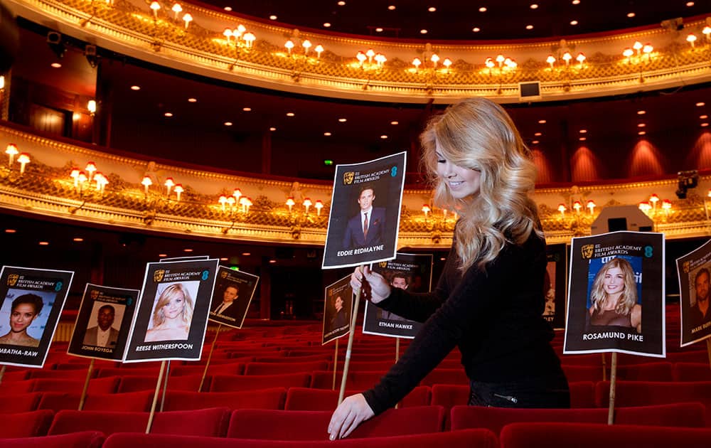Charlotte Martin, a member of the EE British Film Academy staff, poses for photographers with pictures of actors and actresses who are in contention for major BAFTA film awards in the auditorium of the Royal Opera House in London.