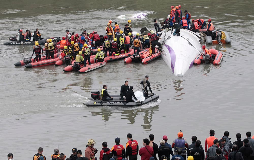 Emergency personnel use a dinghy to bring the body of a passenger in a commercial plane crash to the river shore as others crowd around the plane to rescue other passengers in Taipei, Taiwan.