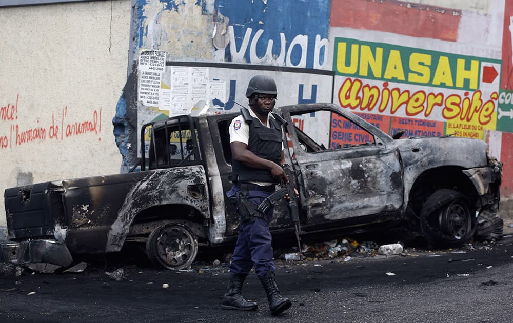 A national police officer walks past the charred remains of a vehicle, set on fire yesterday by students who continued their demands that the government lower fuel prices, in Port-au-Prince, Haiti.