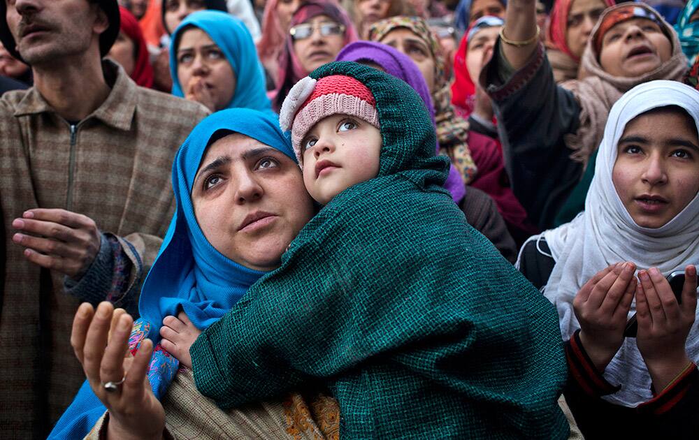 A Kashmiri Muslim woman carries her daughter while praying as the head priest displays a relic of Sufi saint Syed Abdul Qadir Jilani at his shrine in Srinagar.